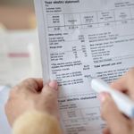 Moteris su rašikliu peržiūri elektros sąskaitos dokumentą