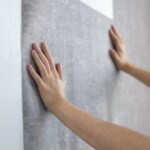 Rankomis prie sienos priglaudžiama pilkų tapetų juosta